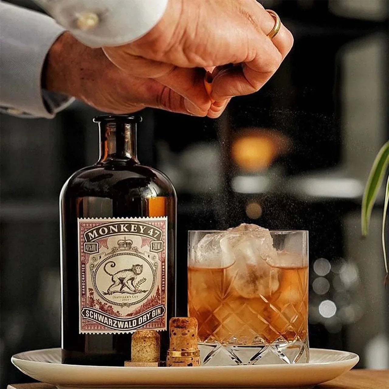 Monkey 47 Schwarzwald Dry Gin bottle with a rocks glass cocktail as orange zest is expressed—hero image for Top 10 Monkey 47 gin cocktails.