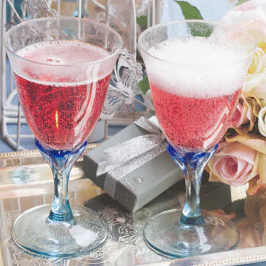 Two glasses of sparking rose on a table with flowers and a bottle.
