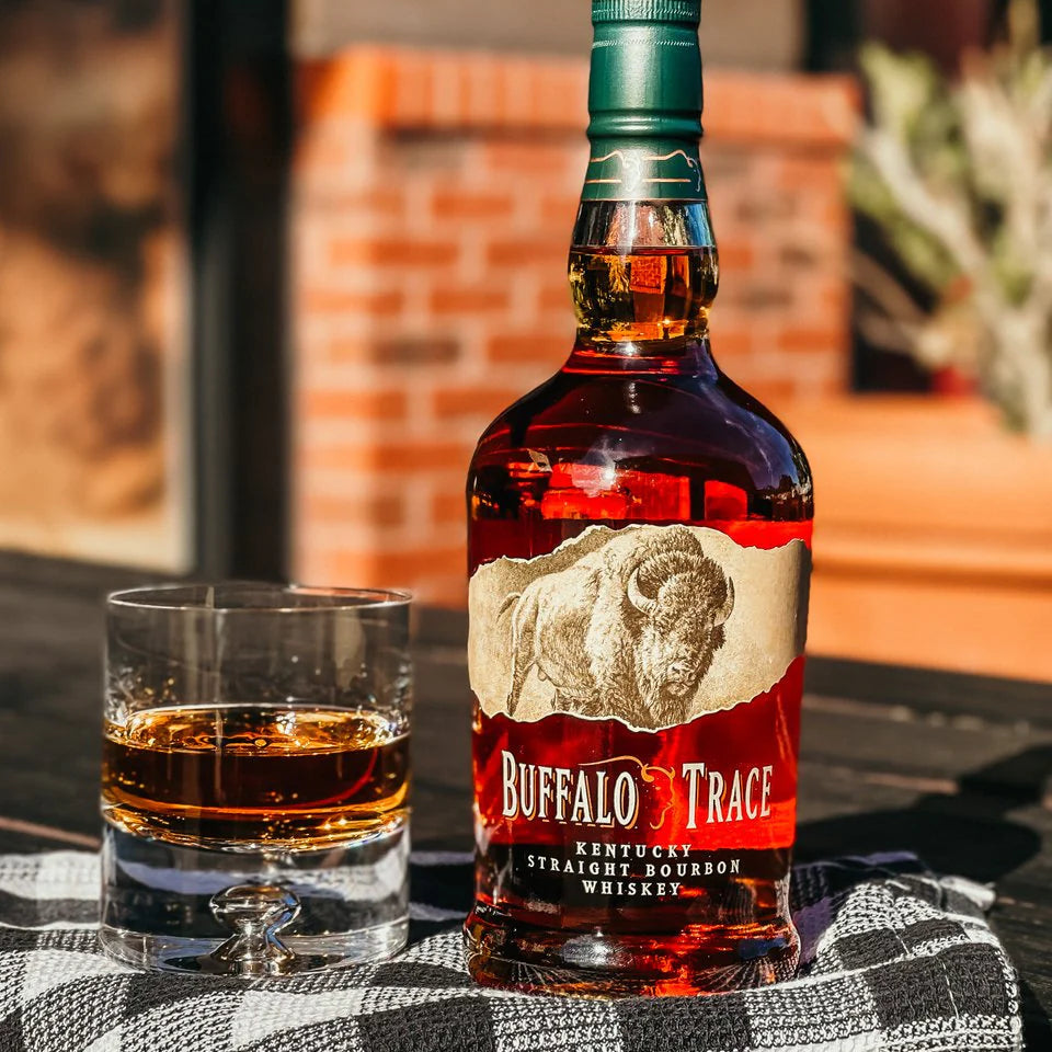Bottle of Buffalo Trace bourbon with a glass of whiskey on a checkered cloth outdoors.