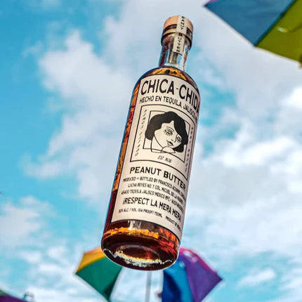 Bottle of Chica Chid peanut butter tequila against a colorful sky background