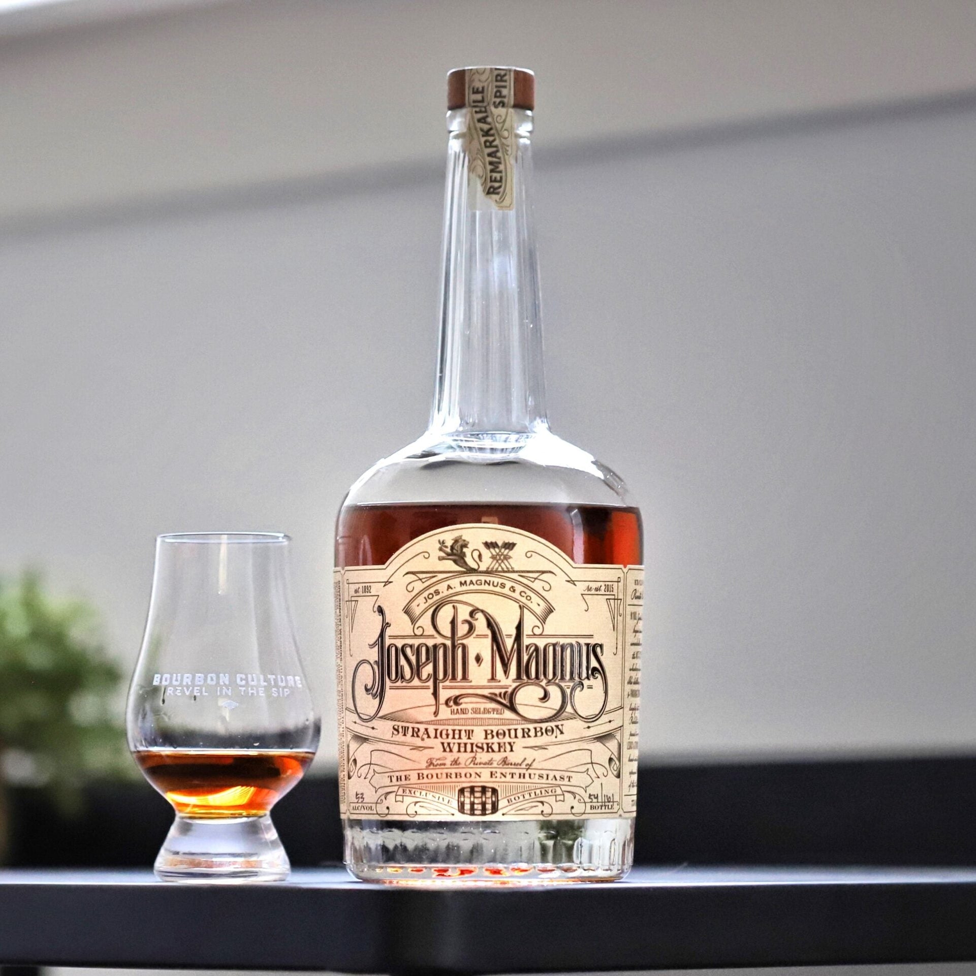 Bottle and glass of Joseph Magnus whiskey on a table with a neutral background