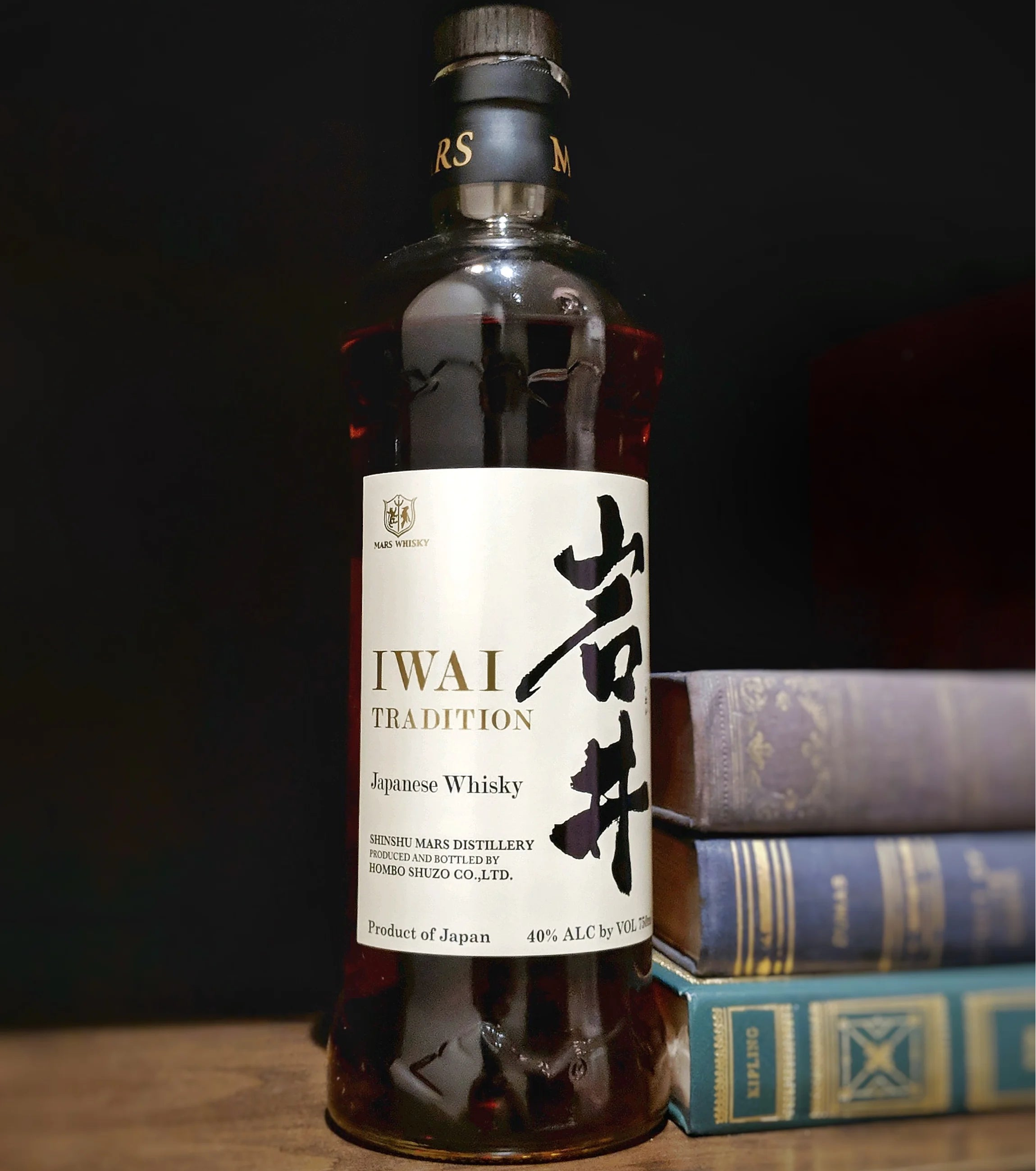 Bottle of IWAI Tradition Japanese Whisky on a dark background with books.