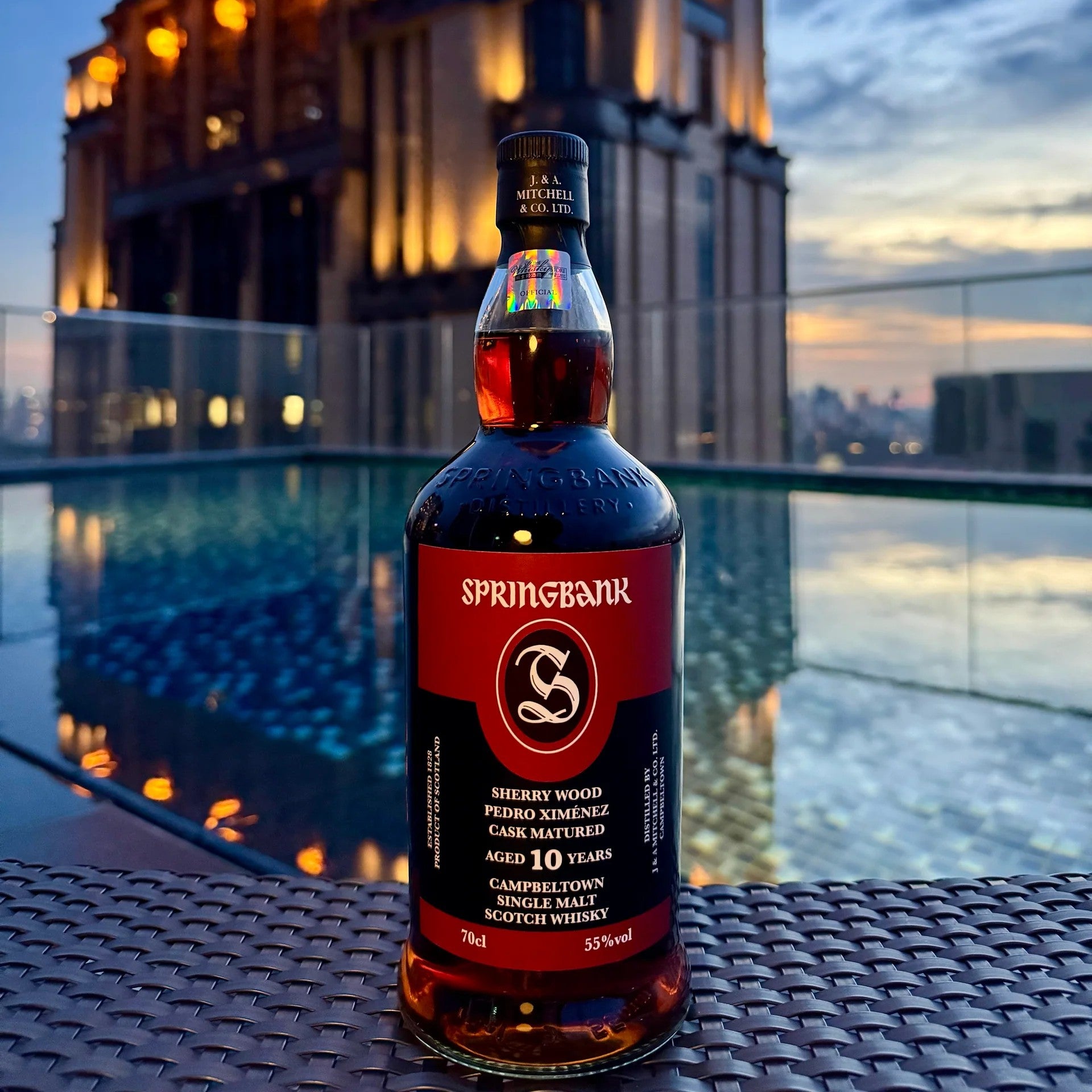 Springbank whisky bottle on a rooftop with pool and cityscape in the background