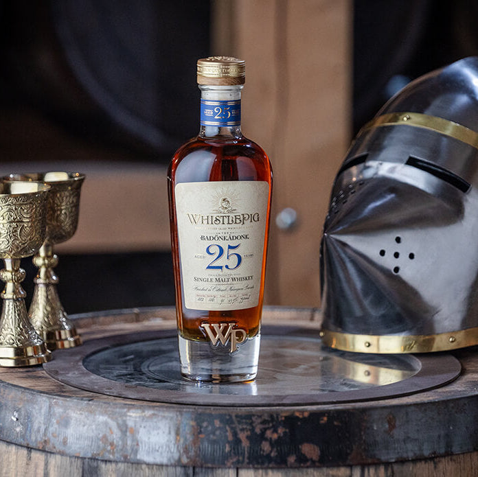 Bottle of whisky on a wooden barrel with a knight's helmet and goblets in the background