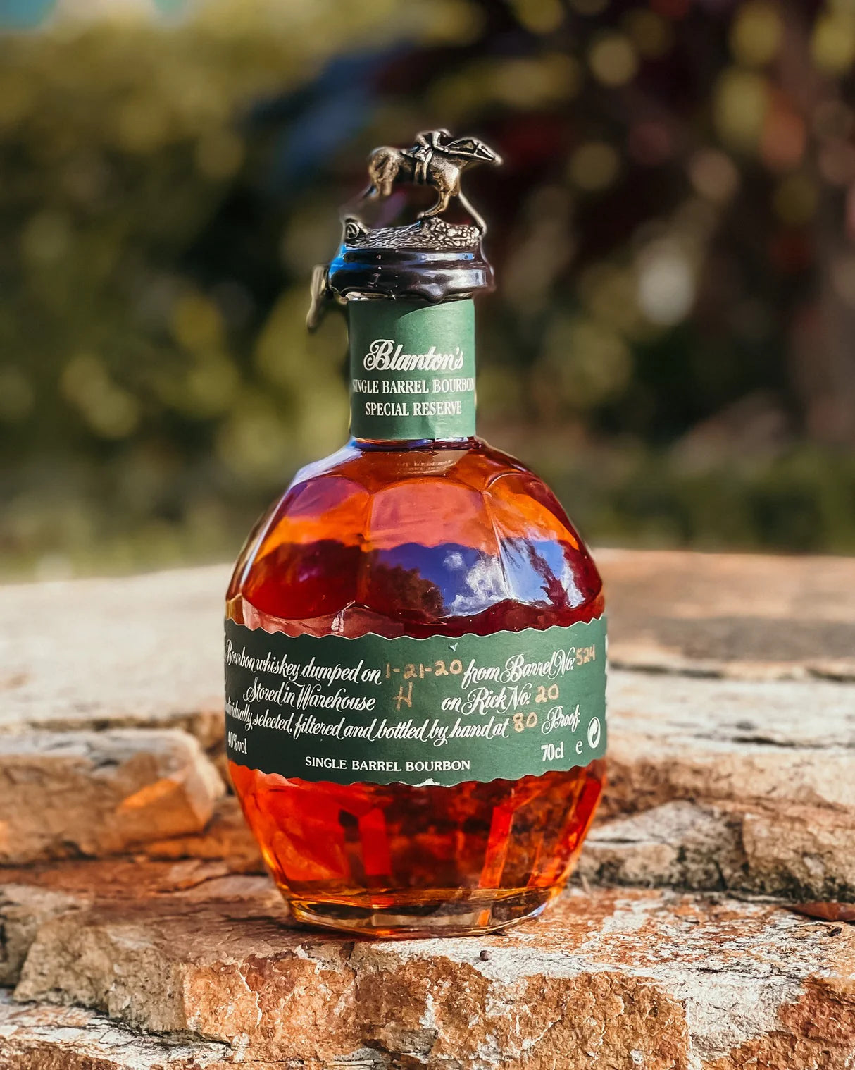 Blanton's Green Label Special Reserve Single Barrel Bourbon bottle outdoors on stone surface, featuring iconic horse and jockey stopper – smooth, mellow Kentucky bourbon whiskey perfect for gifting or collecting.