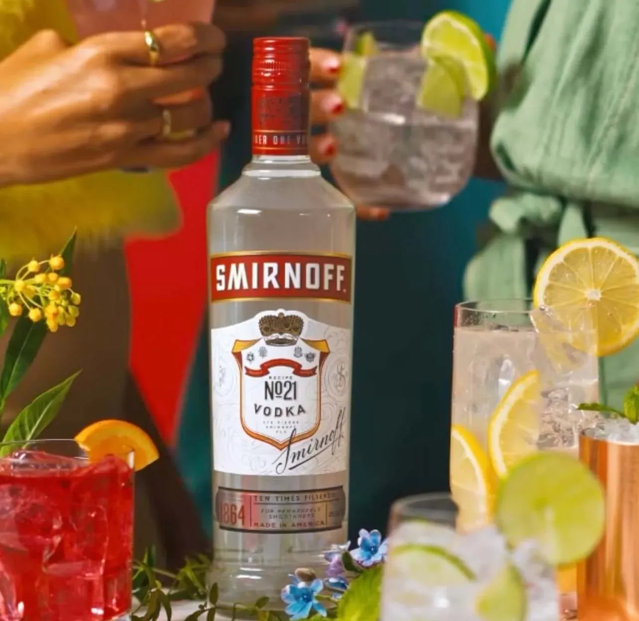 Smirnoff No. 21 Vodka bottle surrounded by cocktails with lemon, lime, and berries at a vibrant gathering