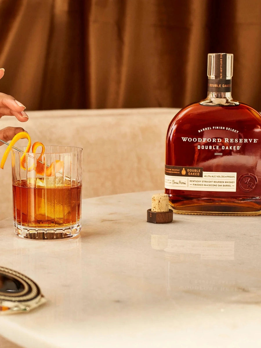 Woodford Reserve Double Oaked Bourbon bottle with Old Fashioned cocktail garnished with orange peel on marble table, premium Kentucky bourbon whiskey.
