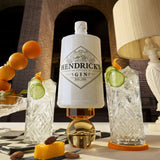 Hendrick's gin bottle with cocktails and garnishes on a table.