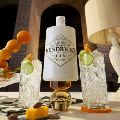 Hendrick's gin bottle with cocktails and garnishes on a table.