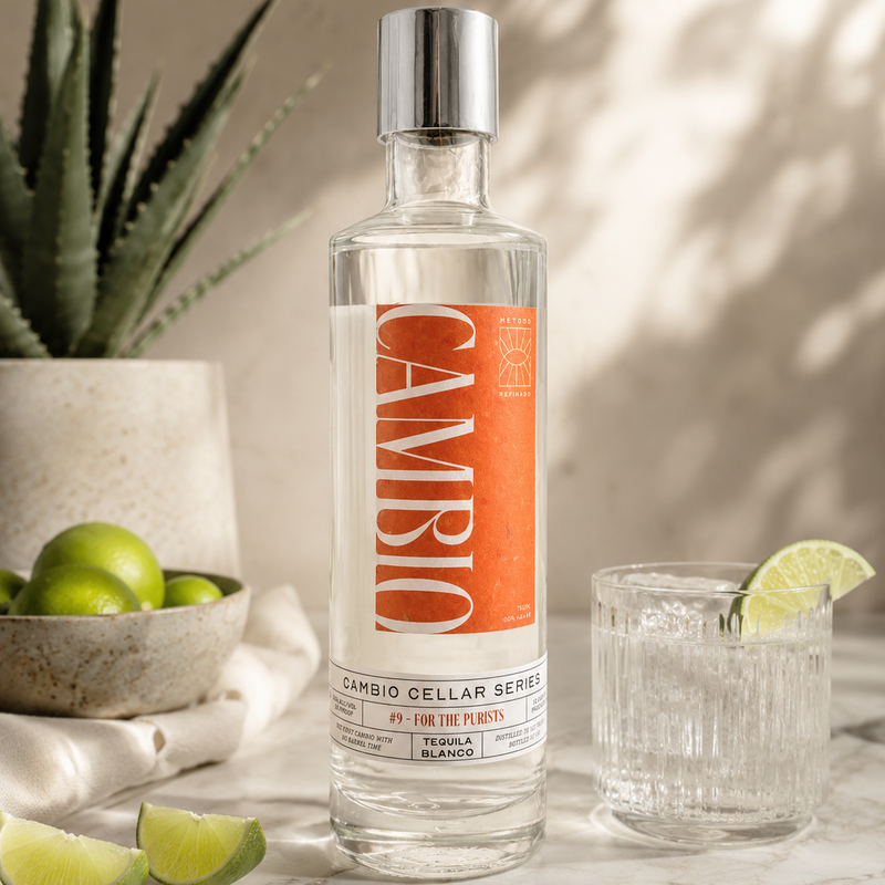 Cambio Cellar Series Blanco tequila bottle with a glass of tequila and lime wedges on a marble surface.
