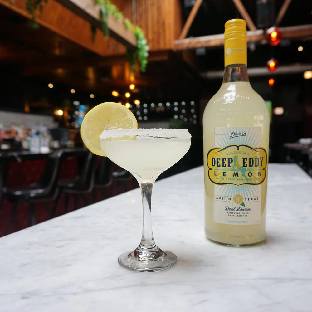 Bottle of Deep Eddy Lemon vodka and a cocktail with a lemon wheel on a bar counter.