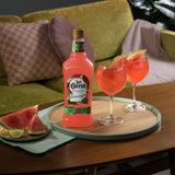 Two glasses of watermelon margarita with a bottle of Jose Cuervo on a wooden table with a green sofa in the background.