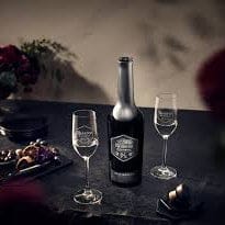 Black bottle with a decorative label on a dark surface with two glasses.