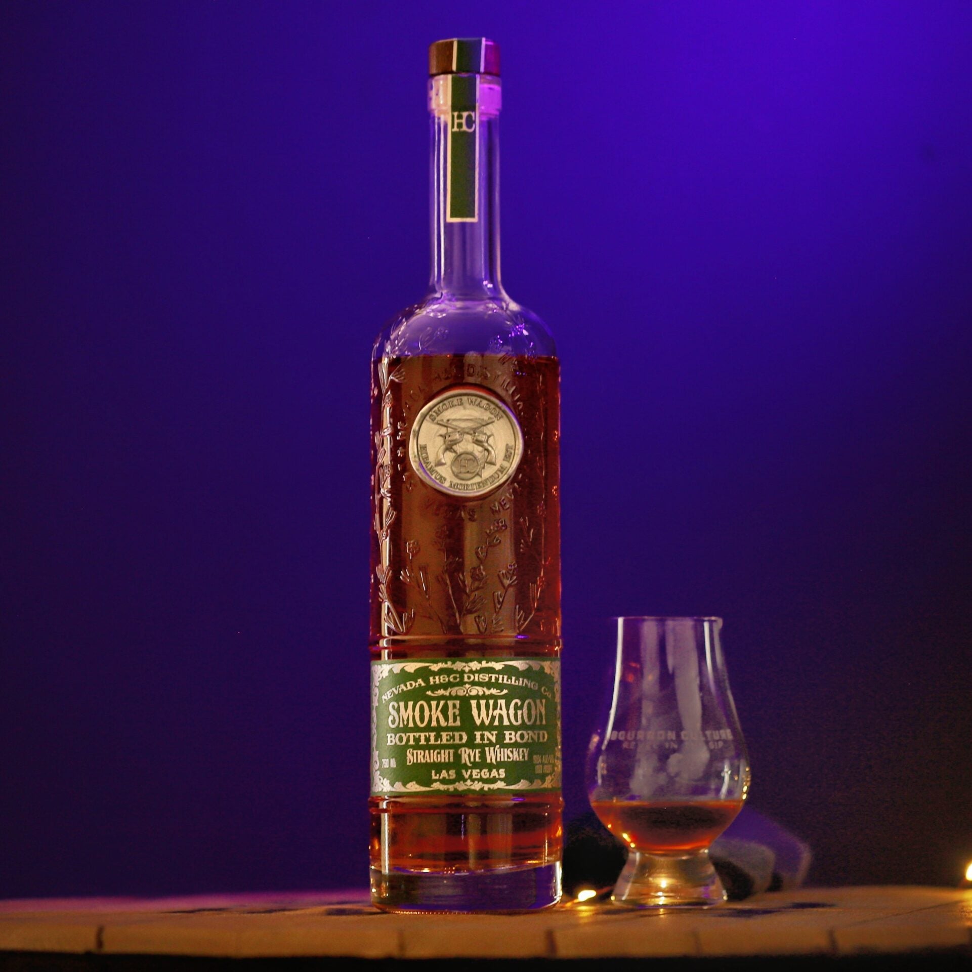 Bottle of Smoke Wagon whiskey with a glass on a wooden surface against a purple background