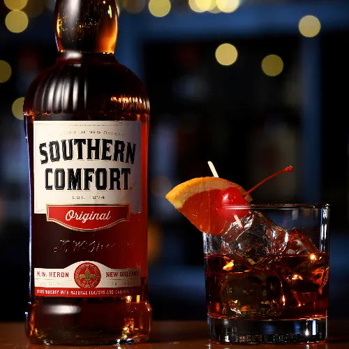 Bottle of Southern Comfort with a cocktail garnished with an orange and cherry on a blurred bar background