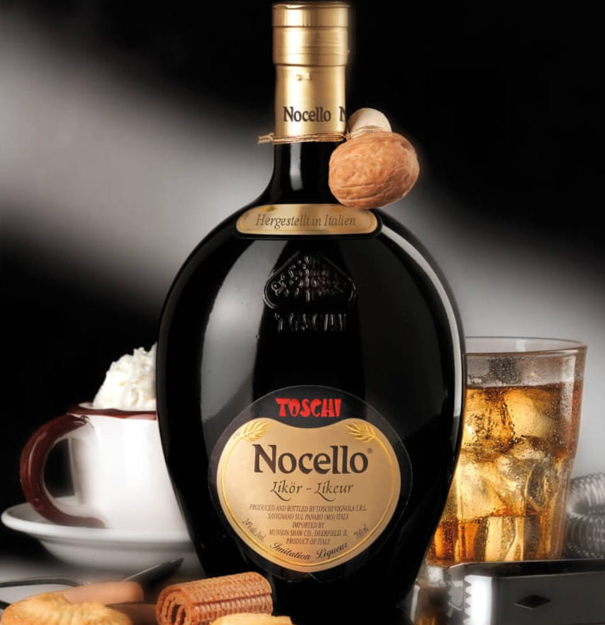 Bottle of Toschi Nocello liqueur with a glass of iced tea and cookies on a dark background