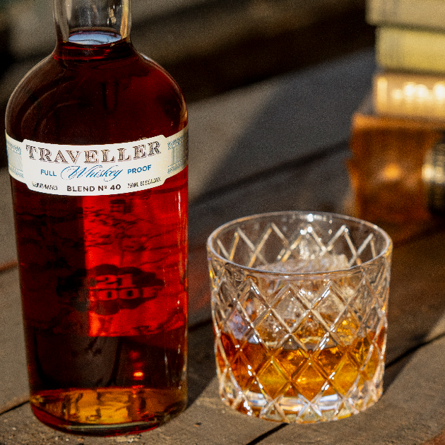 Bottle of 'The Traveller' whisky with a glass of whisky on a wooden surface.