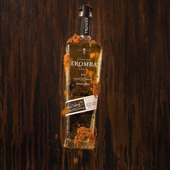 Bottle of Tromba tequila surrounded by sand on a wooden background