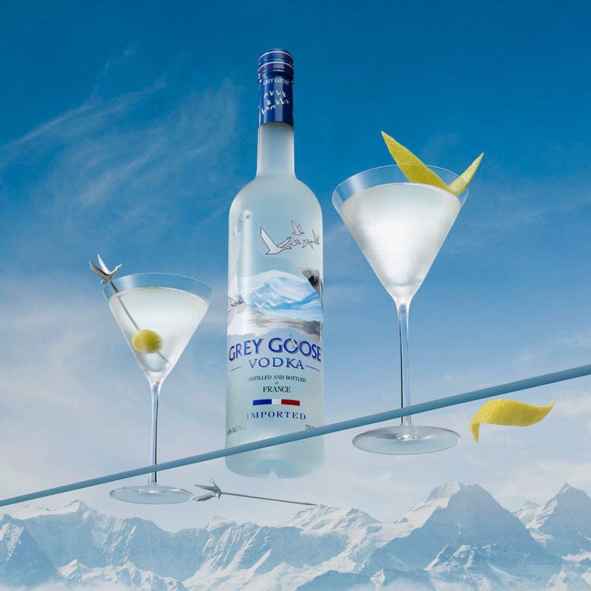 Grey Goose vodka bottle with two martini glasses against a mountainous background