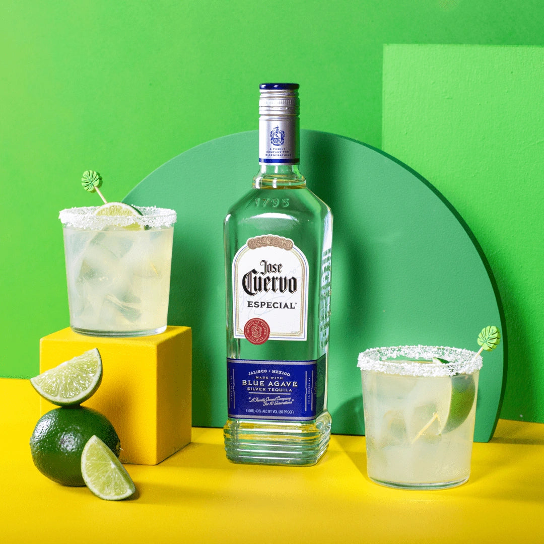 Jose Cuervo Especial Silver Tequila bottle displayed with two margarita cocktails garnished with lime and a bright green and yellow background.