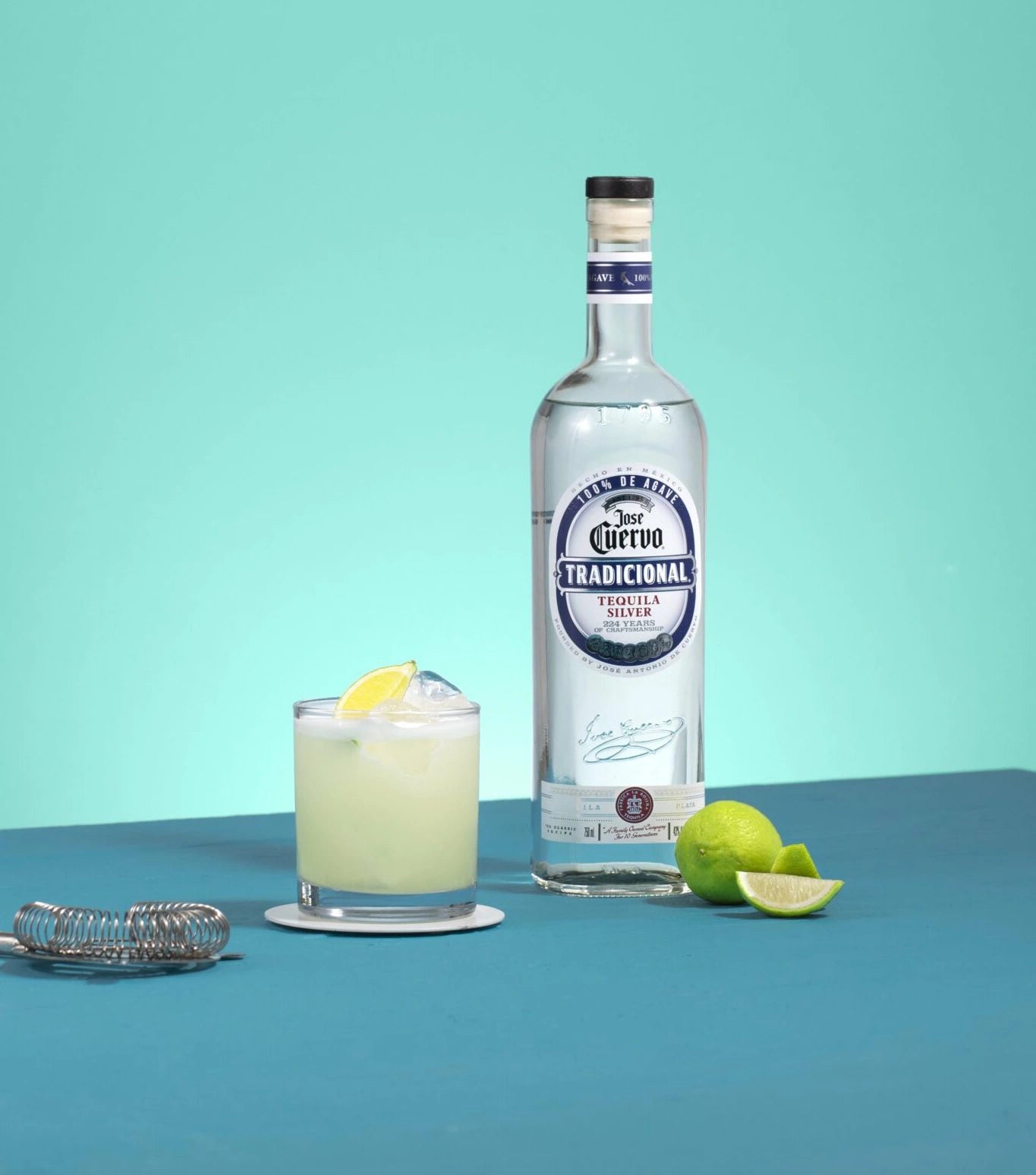 Bottle of Jose Cuervo Tradicional Plata Tequila with a fresh margarita and limes on a turquoise background.