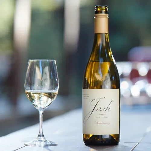 Josh Cellars Chardonnay bottle with a glass of white wine on a table outdoors