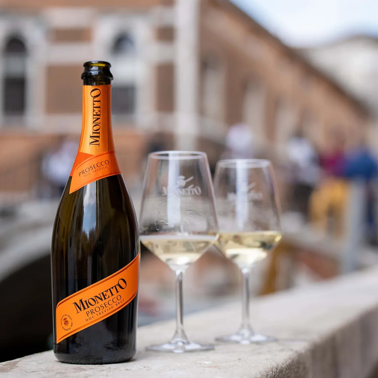 Mionetto Prosecco Brut bottle with two glasses of sparkling wine on a Venetian bridge, crisp Italian sparkling wine