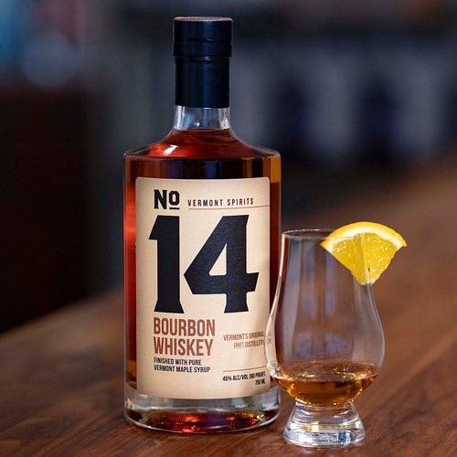 Bottle of No. 14 Bourbon Whiskey with a glass and lemon wedge on a wooden surface.