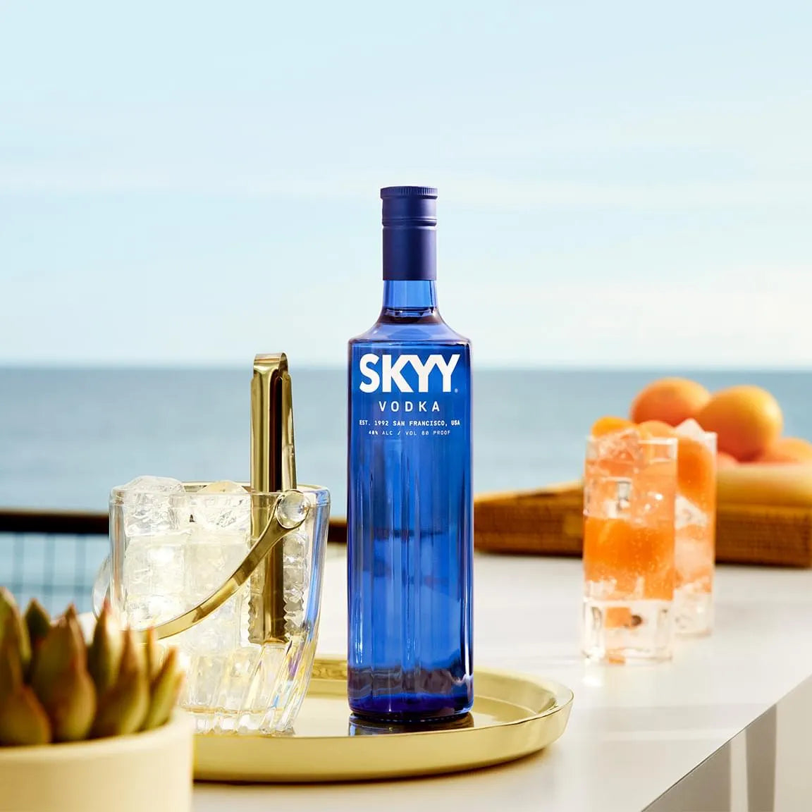 SKYY Vodka blue bottle on patio table with ice bucket and grapefruit cocktails overlooking the ocean