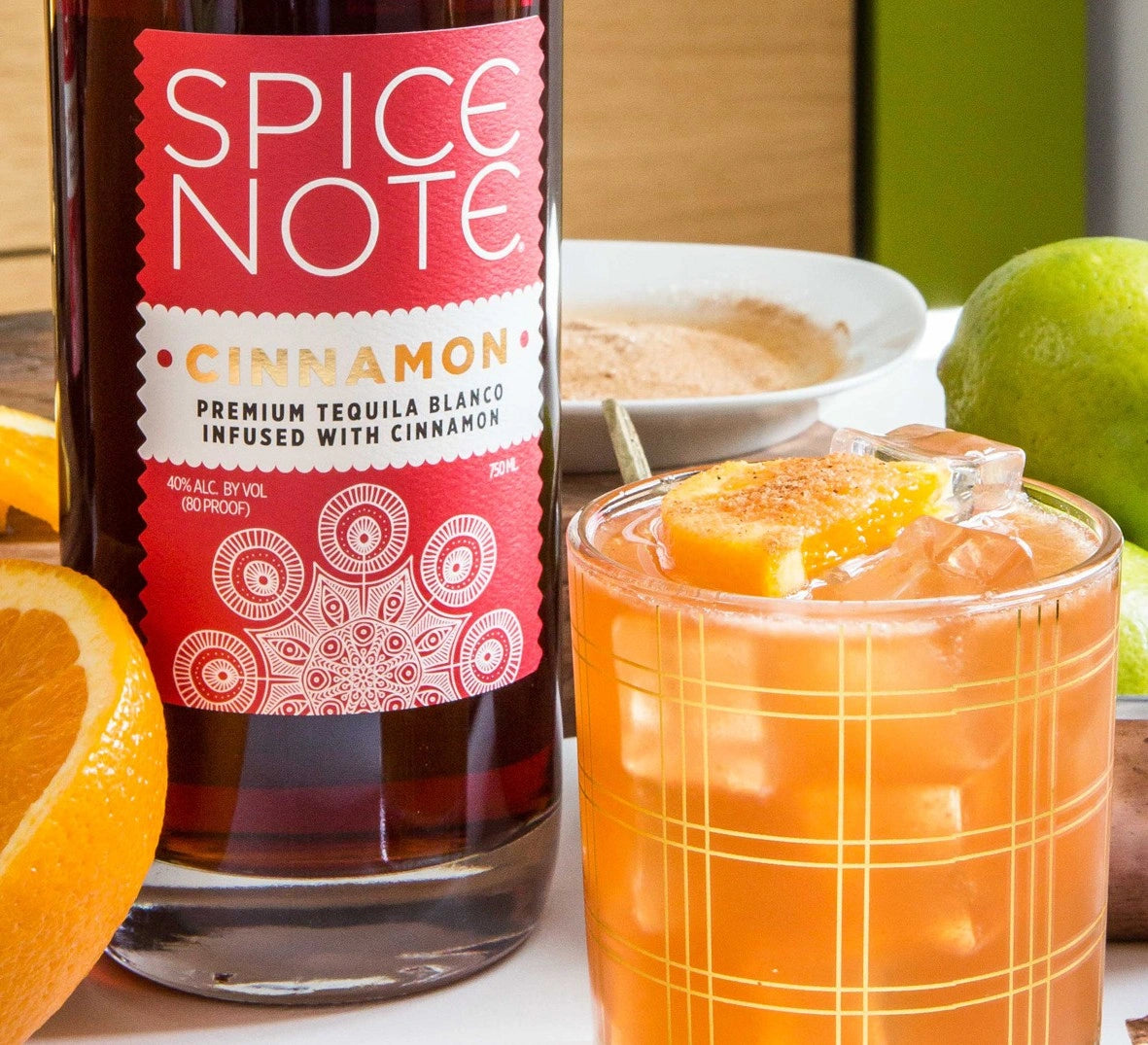 Spice Note Cinnamon Blanco Tequila bottle with a crafted orange cinnamon cocktail, fresh lime and orange garnish in a lifestyle photo.